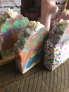 Bars of beautiful multicolored soap named Unicorn Pride. The bars are colored with red, blue, green, yellow, orange and purple with a white base. The tops of the soap are decorated like wispy clouds of soap with a touch of biodegradable glitter.